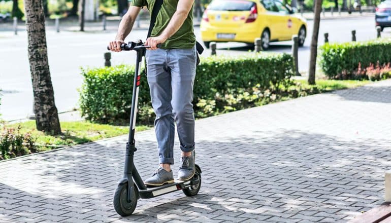 A man rides a scooter down a sidewalk