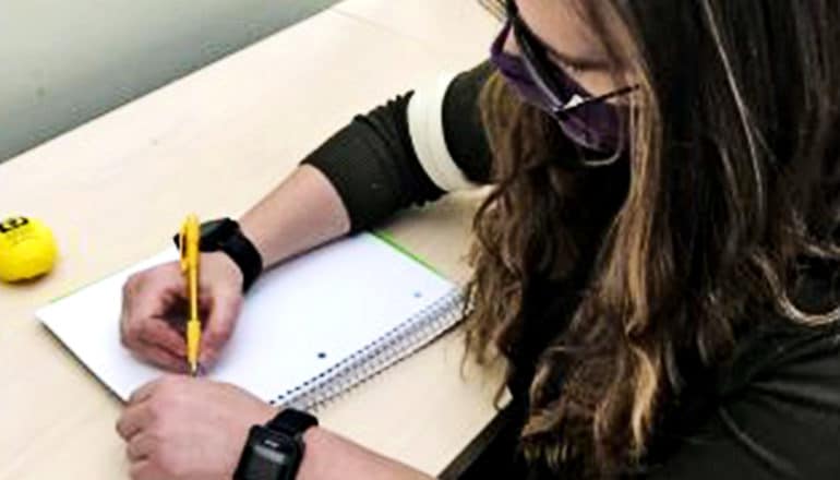 A young woman wears sensor watches on both wrists as she writes with a pen