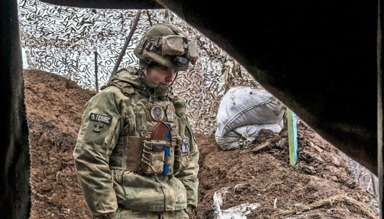 A Ukrainian soldier in a trench near a tent looks down at the ground