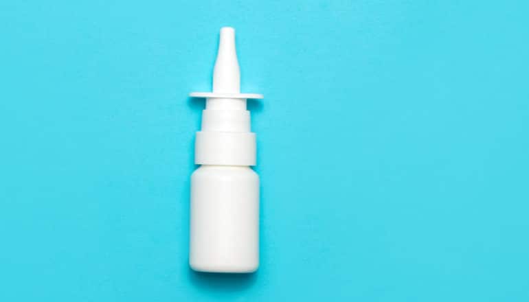 A white nasal spray bottle sits on a blue background