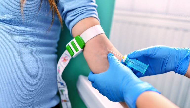 A health care worker draws blood from a pregnant person's arm