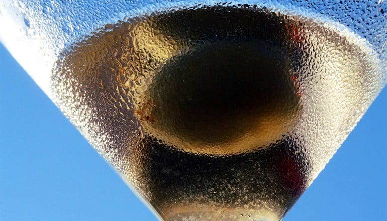 A martini glass holds a drink and olives against a bright blue sky