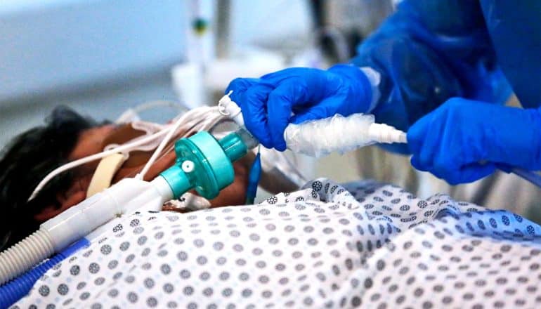 A health care worker checks a COVID-19 patient on a ventilator