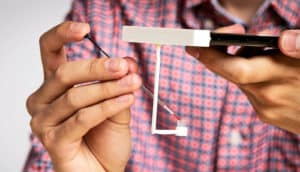 A person pipettes a drop of blood into a container at the end of a short plastic "arm" coming from the phone-mounted device