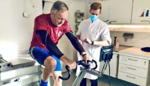 A study participant rides a stationary bike as a research checks his watch