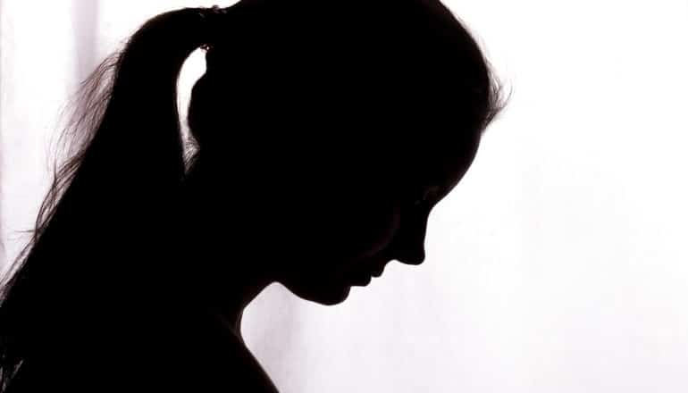 A teen girl looks downward in silhouette