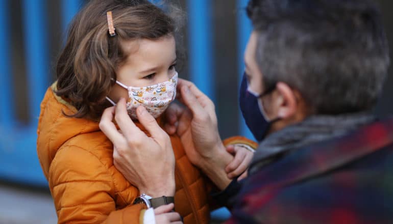 adult adjusts small child's mask