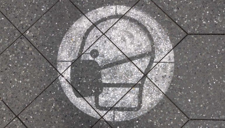 A sign on the sidewalk shows a person wearing a mask