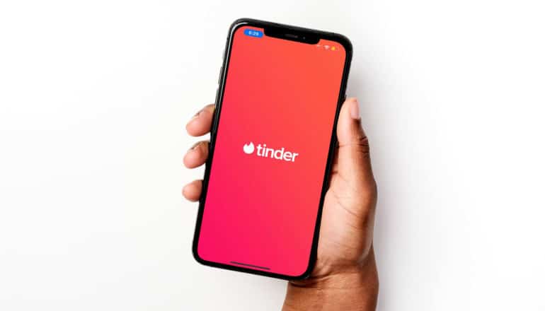 hand holds phone showing tinder app logo