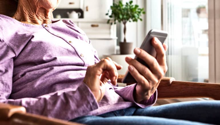 An older woman sitting in a chair looks down at her smartphone