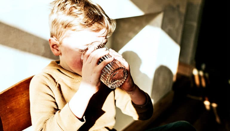 A young boy drinks a glass of water at a table with both hands