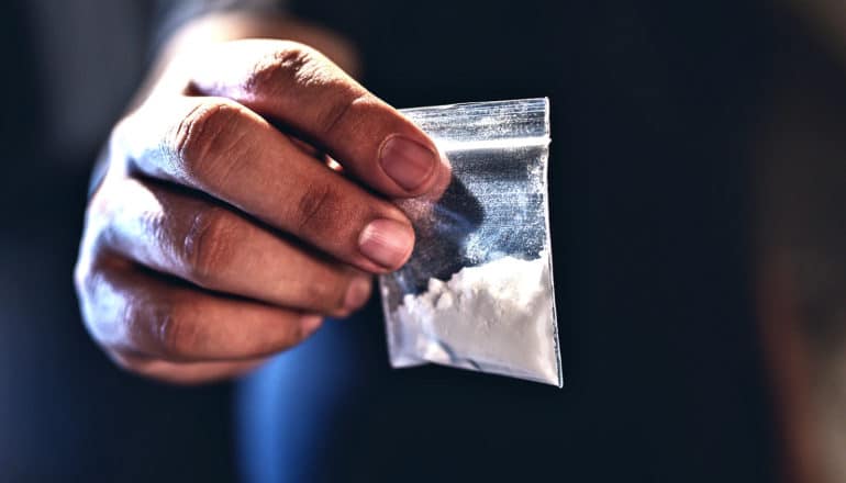 A man holds a small baggie filled with white powder