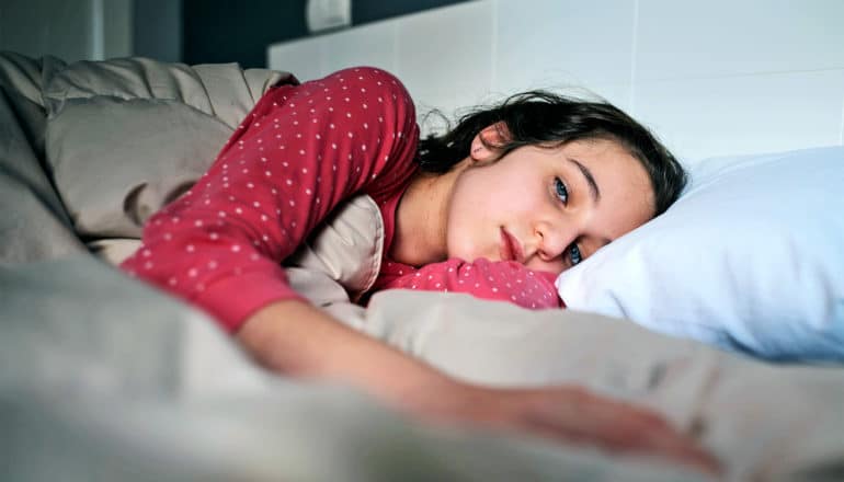 A teen girl has a blank expression while lying in bed