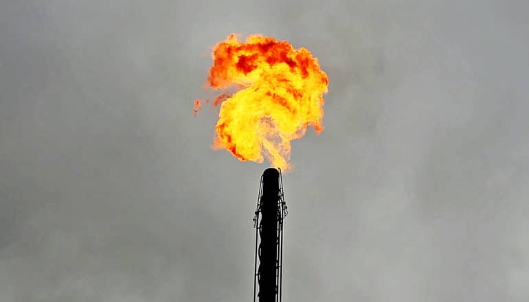 A fiery plume of flared natural gas comes from a smokestack against a gray sky