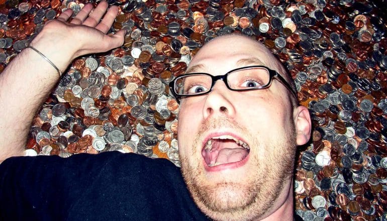 A man makes a surprised, excited face while laying on a huge number of coins