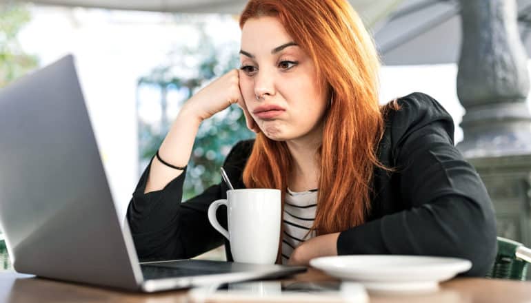 woman looks disappointed at laptop screen