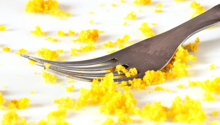 A fork on a white plate surrounded by yellow cake crumbs