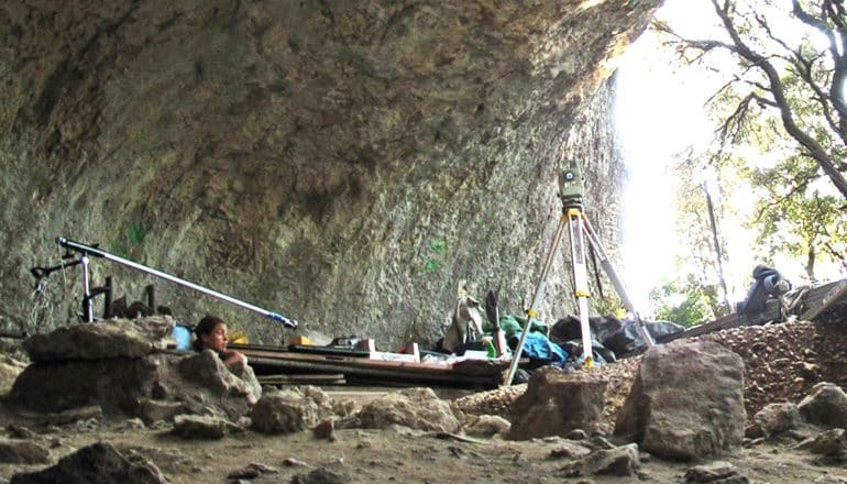 Researchers dig in a cave, with one poking her head out of a hole