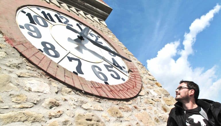 A man looks up at a large clock on a stone tower