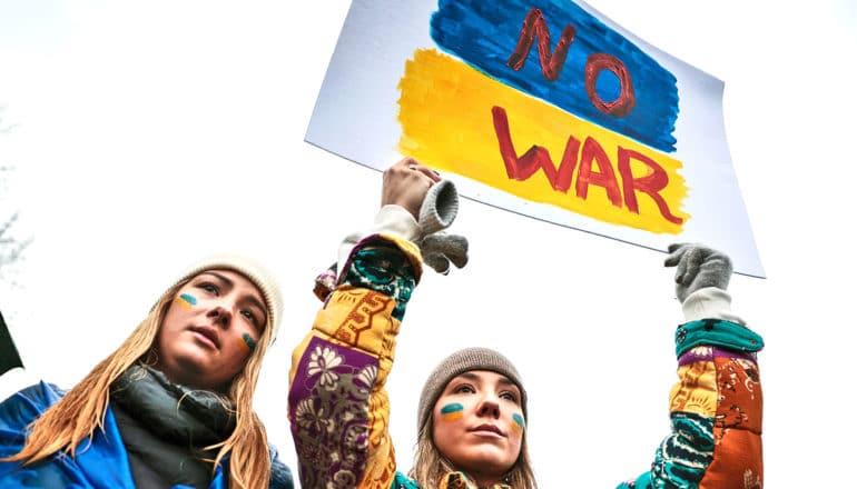 Young protesters hold a sign that reads "No War" and shows the colors of the Ukrainian flag