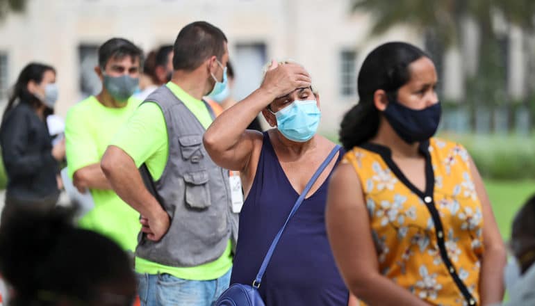 masked person in line holds hand to forehead