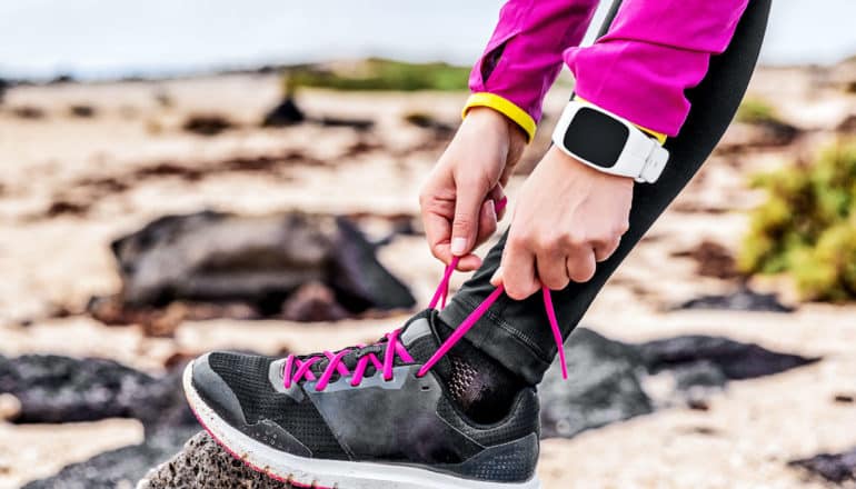 A woman ties her running shoes while wearing a wearable sensor watch