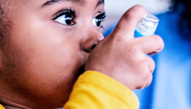 A little girl uses her asthma inhaler