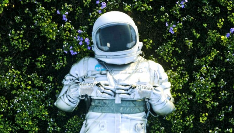 An astronaut lays down in a field of green plants