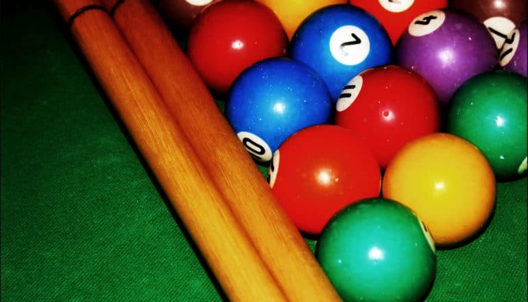 Billiards balls of different colors sit next to two cues on a green table