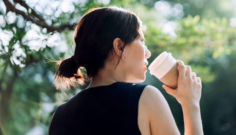 A woman walks through a park while sipping coffee