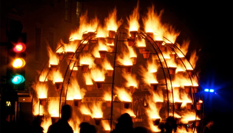 A metal globe has several buckets with fires in them covering it