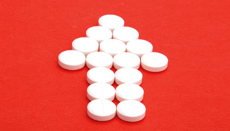 White pills on red background form the shape of an arrow pointing upward