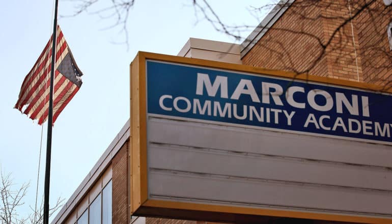 sign for Marconi Community Academy in front of tattered US flag