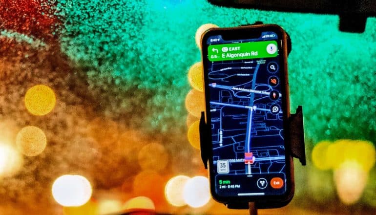 A phone attached to a windshield shows a map app's GPS route