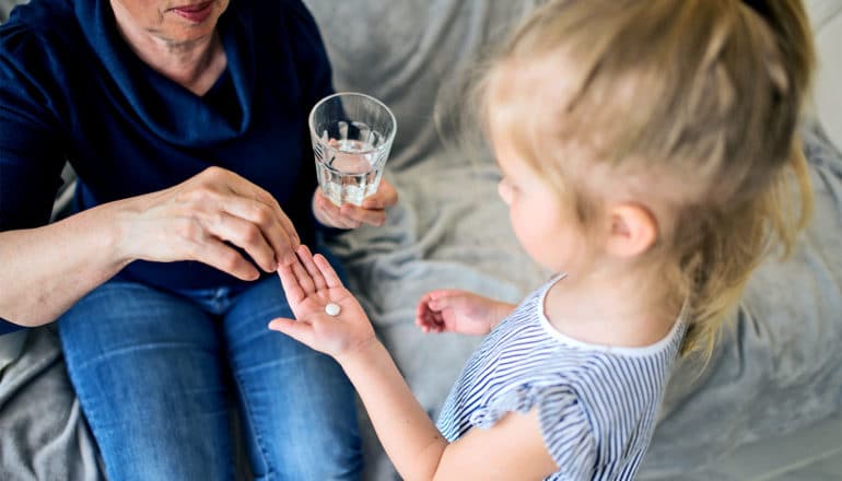 A grandmother hands her granddaughter pills and a glass of water