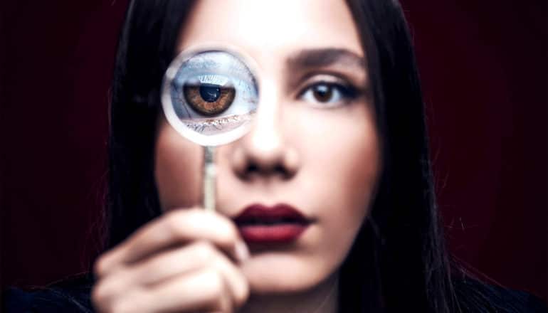 A woman holds a magnifying glass up to one eye