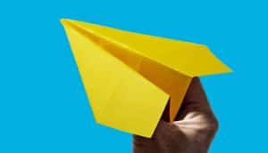 A person holds a yellow paper airplane against a blue background