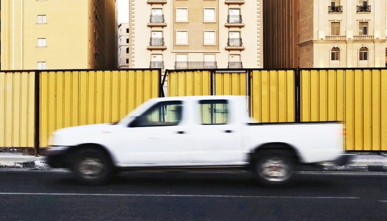 blurry white pickup truck drives past yellow wall