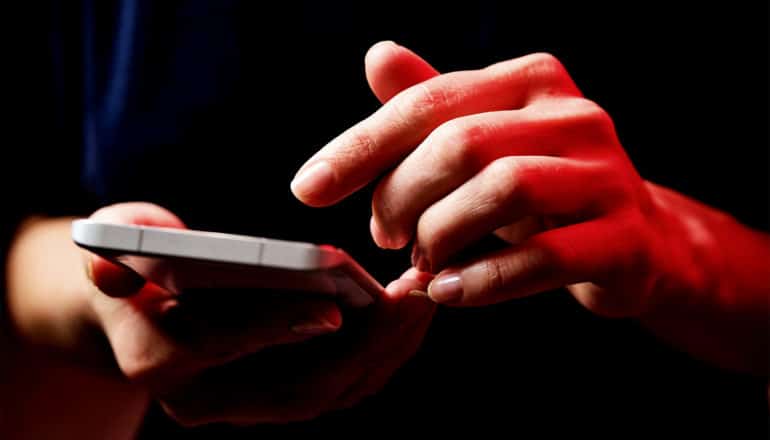 A woman scrolls on her phone while red light shines on her hand