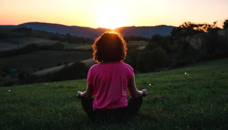 person in seated meditation posture outdoors at sunrise