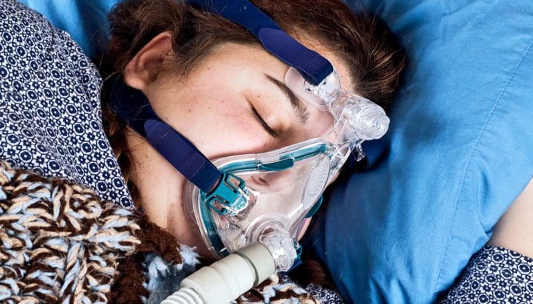 A woman sleeps while wearing a CPAP mask for treating sleep apnea