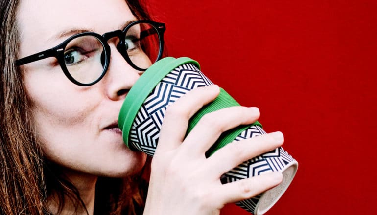 A woman drinks from a reusable coffee cup against a red background