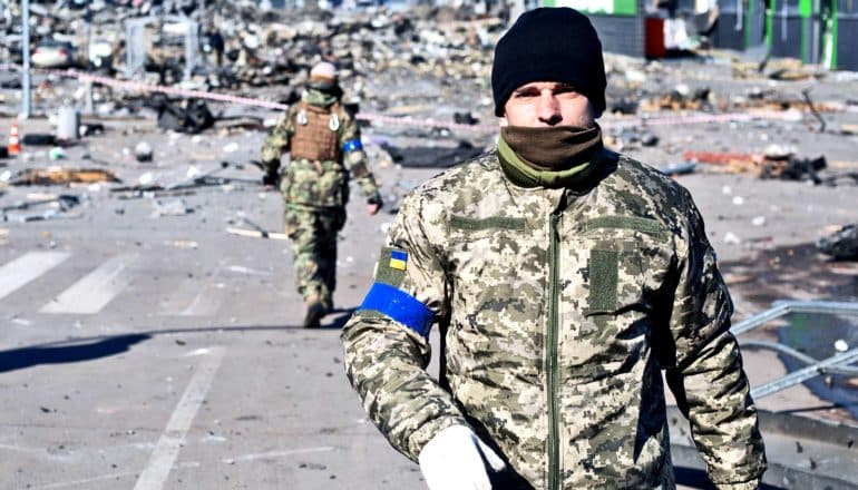 Ukrainian soldiers walk down a city street covered in rubble