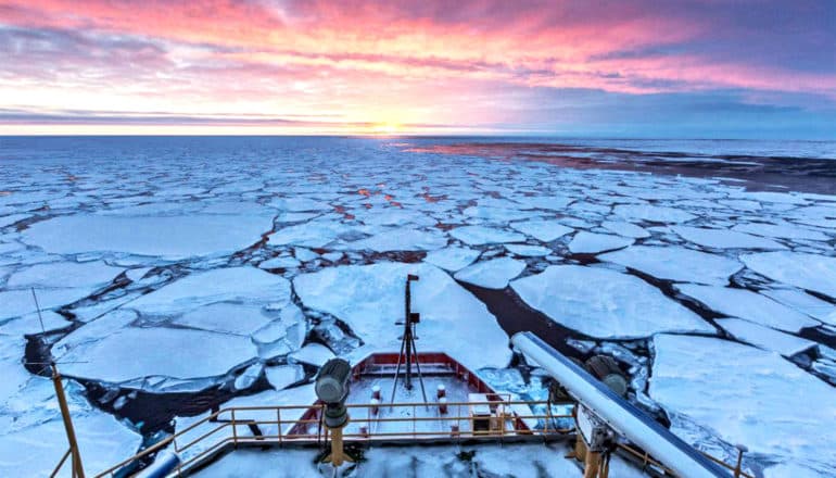 The researchers' ship breaks moves toward the horizon, breaking through a huge chunks of sea ice, as the sun rises and illuminates the distant clouds