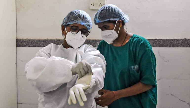 two health care workers, one putting on PPE suit