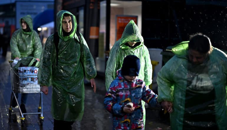 people in ponchos walk on street at night