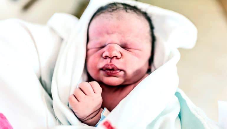 A newborn baby wrapped in a white hospital blanket