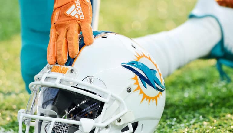 A football player touches a gloved hand to the forehead of a football helmet while kneeling on the field