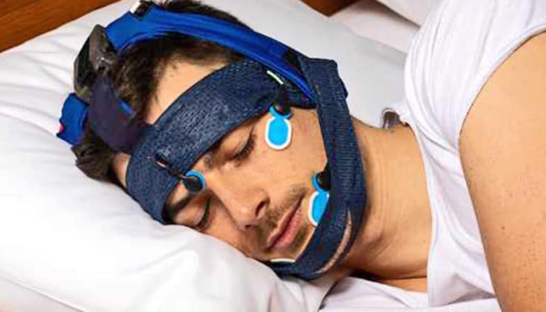 A man wears the SleepLoop system on his head and face, which wraps around the top of his head, forehead, and chin.