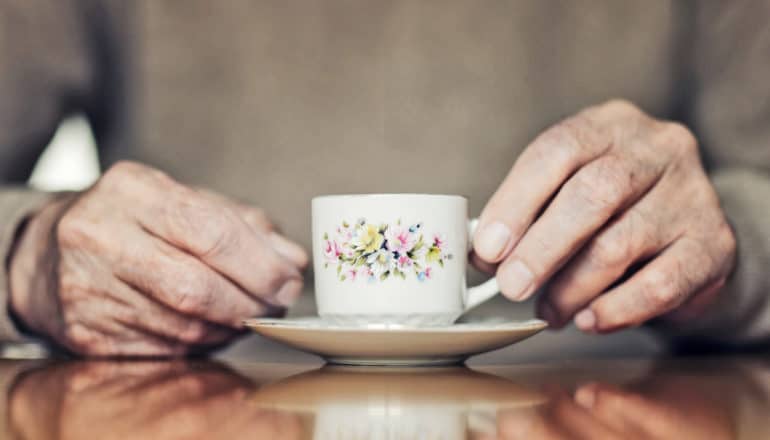 elderly person's hands hold small floral teacup